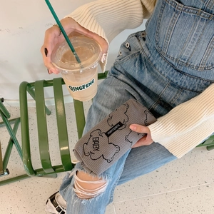 Close-up of grey corduroy pencil case with cartoon bear held by a model on a green bench