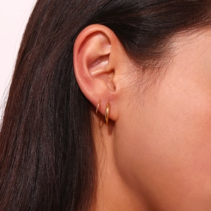 Détail de boucles d'oreilles doubles créoles plaquées or 18 carats portées par une femme
