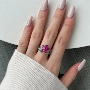 Detail of a floral S925 silver ring featuring pink gemstones and green leaves on a hand