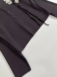 Detail of dark grey ribbed knit cardigan featuring matching buttons and white flower accent