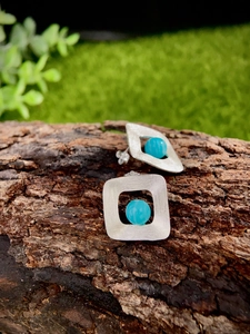 Detail of silver S925 square stud earring with blue stone set on natural wood bark