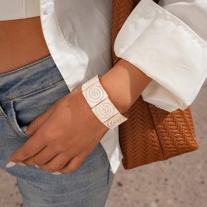 Detail view of a wide gold-tone link bracelet with white enamel and golden spiral patterns