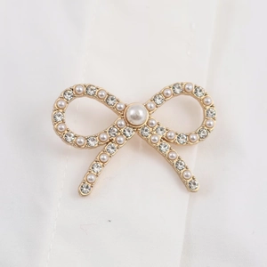Detailed close-up of a golden bow brooch with white pearls and crystals on a white shirt