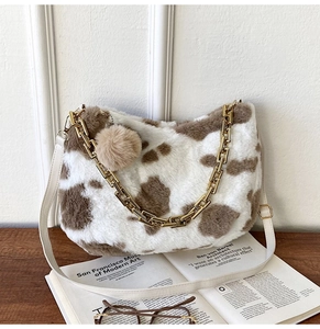 Detail of cow print plush tote with metal chain strap and pompom charm on artistic books
