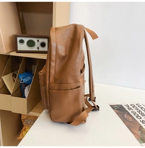 Side view of a brown PU leather backpack on a minimalist desk with home decor items