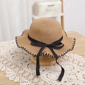 Close-up detail of woven straw sun hat with black ribbon bow and wavy brim edge decoration