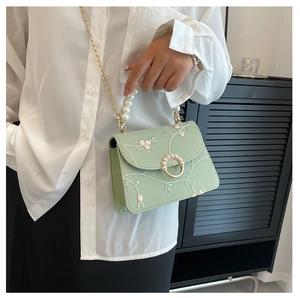 Detail of floral embroidery on light green handbag with pearl handle and chain strap