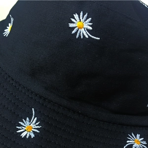 Close-up of white daisy embroidery and stitching on black cotton bucket hat fabric
