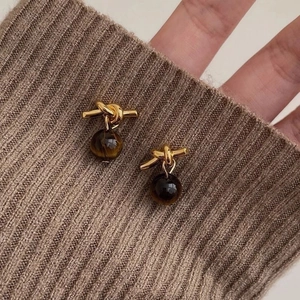 Detail of gold knot hoop earrings with brown gemstone beads on a knit sweater cuff
