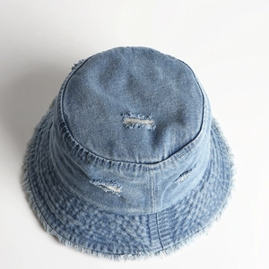 Detailed view of light blue distressed denim bucket hat with frayed edges and ripped effects