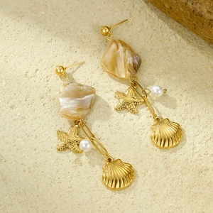 Ocean-themed gold starfish earrings with white pearls and shell pendants on stone