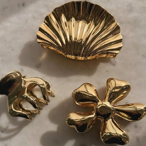 Three-piece gold metal hair claw set featuring shell and flower designs on marble