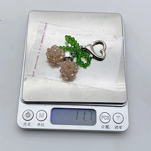 Detail shot of a handmade crystal cherry keychain showing its weight of 11.7g on a digital scale