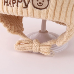 Detail einer cremefarbenen Baby-Strickmütze mit Bärenstickerei und Winterstruktur