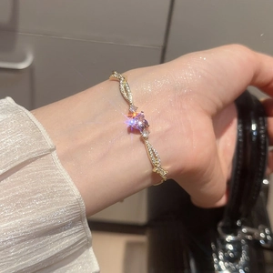 Detail of adjustable gold heart bracelet with purple stone and shimmering zircon accents