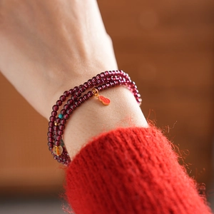 Close-up of multi-layer garnet bead bracelet with golden charms on model's wrist