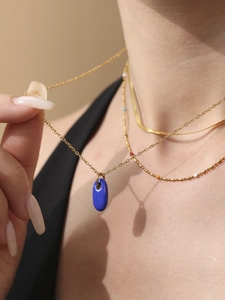 Detailansicht einer blauen Emaille-Halskette mit goldener Schichtkette an einem Model