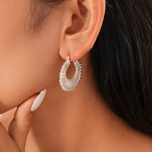 Close-up of silver woven hoop earrings with intricate metal coil design on model