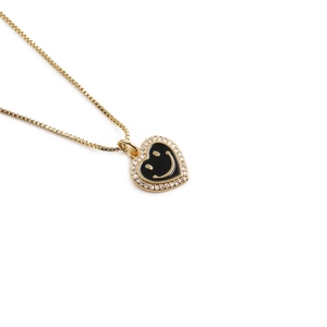 Detail of gold heart pendant with black enamel smiley face and cubic zirconia stones