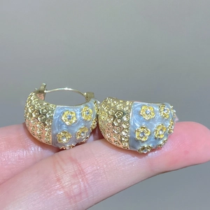 Macro view of gold flower earrings with purple enamel and zircon inlay detail