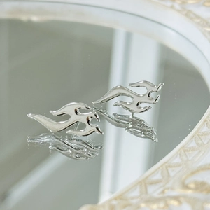 Macro shot of silver flame earrings with a polished mirror finish on a reflective mirror