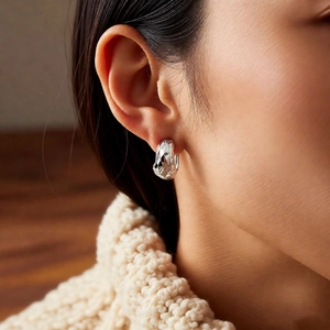Close-up of a silver quilted U-shape hoop earring worn by a model in warm lighting