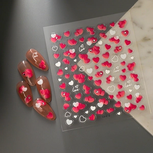 Detailed view of 3D heart nail art stickers and finished manicure tips on marble surface
