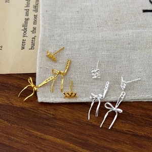 Elegant gold and silver bow stud earrings on vintage newspaper and linen background
