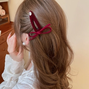 Detail of red velvet bow hair clip with metallic smile charm worn on hair