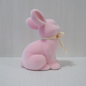 Close-up of a pink flocked Easter rabbit ornament with a cream ribbon on a wood surface