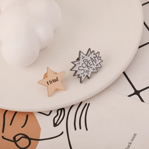 Detail shot of enamel pins featuring 'I tried' star and 'SCREAM' bubble on a white tray