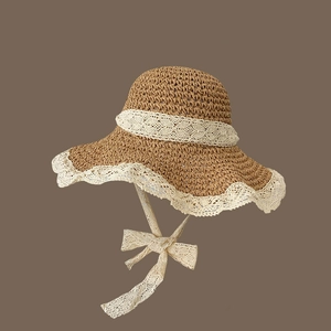 Close-up of brown straw sun hat with delicate white lace trim and adjustable lace bow tie