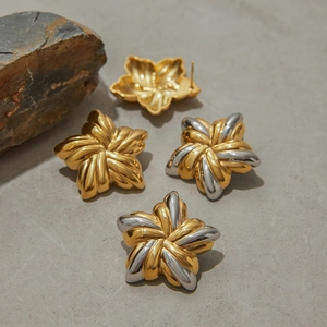 Detailansicht von blumenförmigen Ohrringen in Gold und Silber auf einem Steinhintergrund