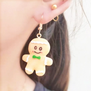 Close-up of handmade gingerbread man earrings with green bow tie on earlobe