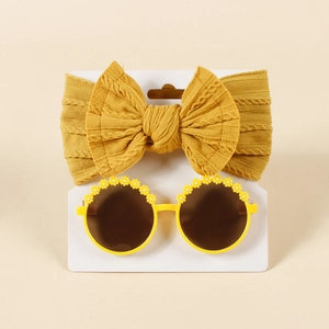 Nahaufnahme von gelbem Strick-Stirnband mit Schleife und Gänseblümchen-Sonnenbrille auf Karte