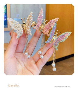 Detail view of butterfly hair clips with imitation pearls and hanging gold tassels in three colors