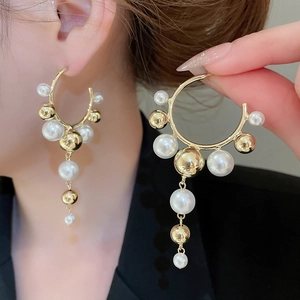 Detailed view of C-shape gold pearl earrings with long tassels on a model for elegant style