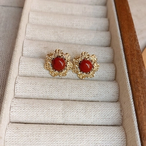 Detail view of gold flower earrings with red beads in a beige jewelry box tray