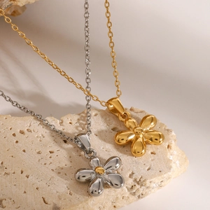 Gold and silver 18k plated stainless steel flower pendant necklaces on beige rock