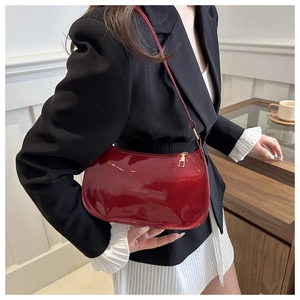 Model wearing a red patent leather half-moon baguette bag with elegant gold hardware details