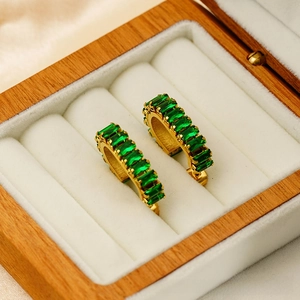 Macro shot of U-shaped gold huggie earrings with emerald-green cubic zirconia stones