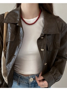 Détail du collier de perles rouges vintage porté avec une veste en cuir marron