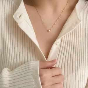 Close-up of a minimalist gold heart pendant necklace worn on a beige knit sweater