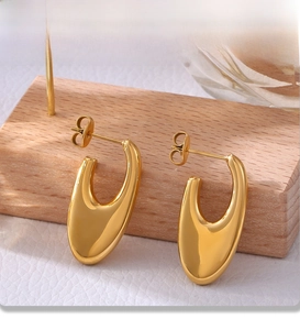 Close-up of gold PVD plated U-shaped earrings showing polished mirror finish on wood