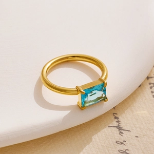 Detailed macro view of 18K gold-plated ring with square blue gemstone on vintage paper