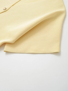 Detailed close-up of fine pale yellow knit texture with a polished gold button detail