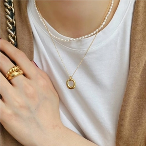 Close-up of layered gold hoop necklace and pearl strand necklace on model with rings