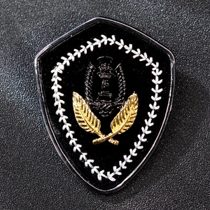 Macro shot of shield-shaped brooch with silver border and gold embroidery on black background
