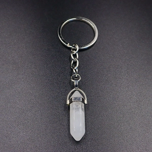 Close-up of hexagonal white crystal bullet pendant with silver metal keychain on grey surface