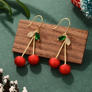 Detail of red cherry earrings with gold stem and leaf on a wooden stand